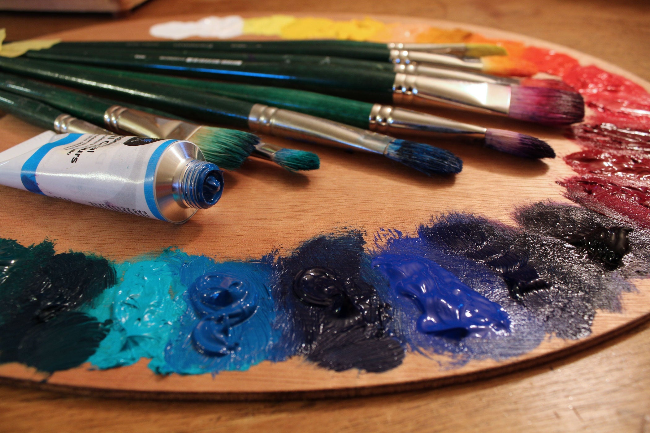 Artist paint brushes on wooden palette. Texture mixed oil paints
