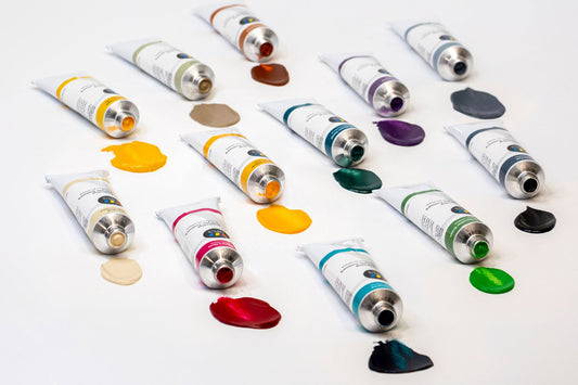 All 12 of the new Opus Essential Acrylic Colours paints are squeezed out in front of the tubes on a white canvas surface.