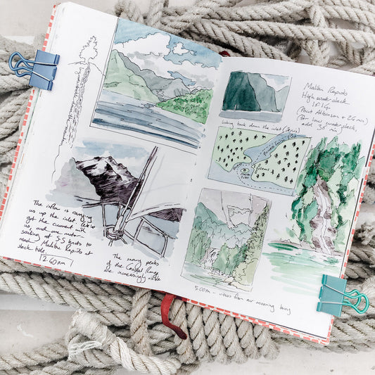 Artist Andrea England's open sketchbook filled with watercolour landscape studies, hand-drawn maps, and travel notes, resting on coiled rope.