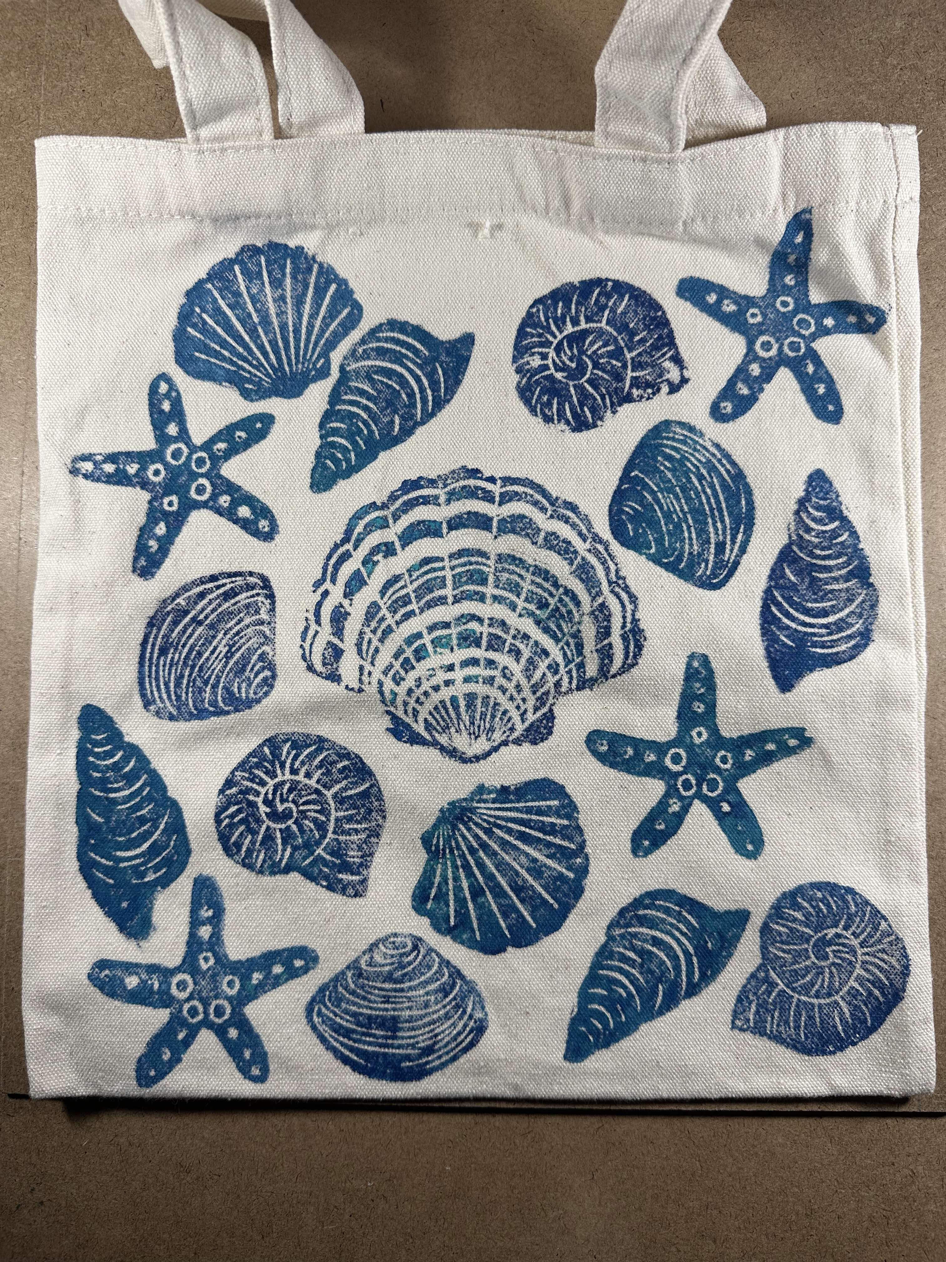 Cotton tote bag decorated with handmade lino printed seashell and starfish designs using soft carving blocks and fabric paint.