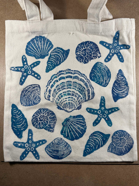 Cotton tote bag decorated with handmade lino printed seashell and starfish designs using soft carving blocks and fabric paint.