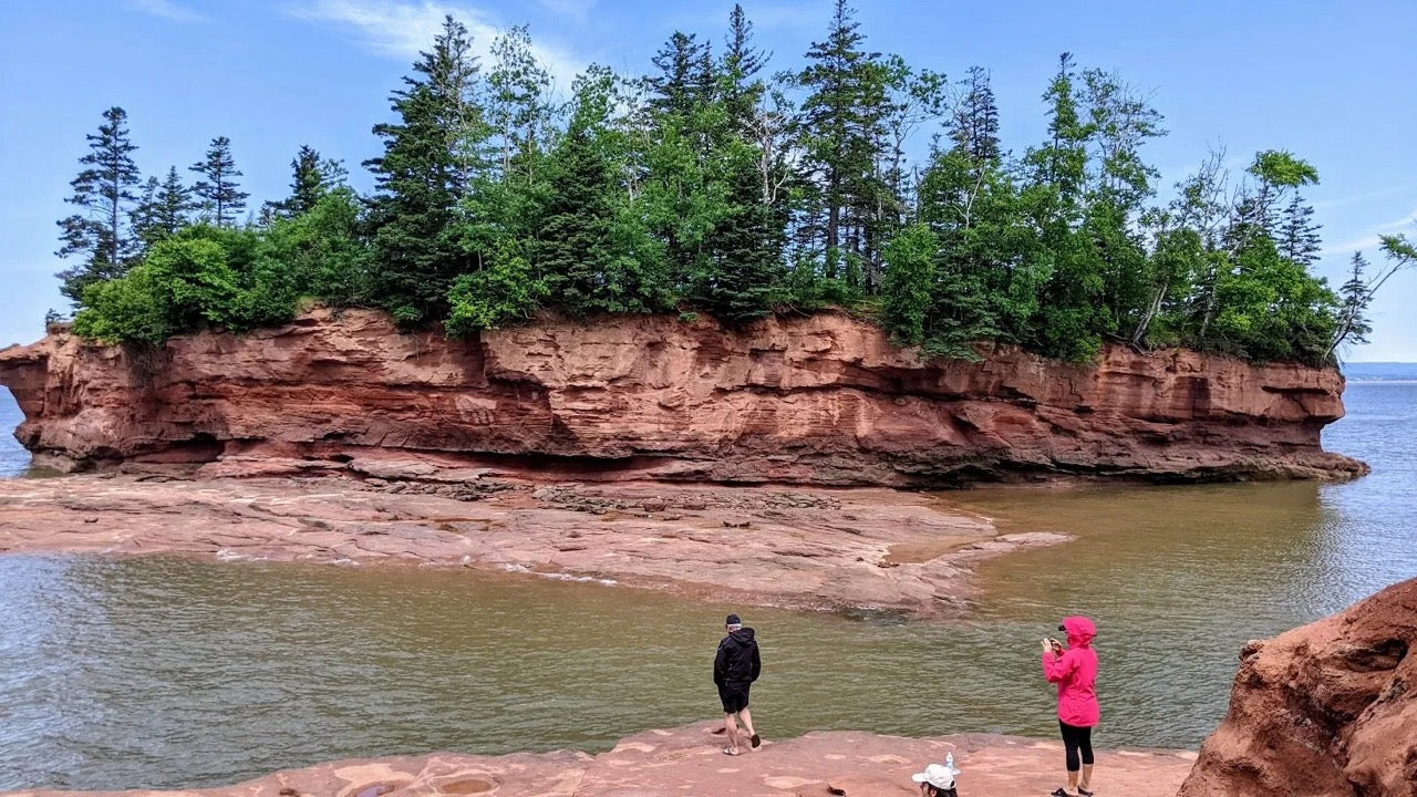 Image of  two people on the shore in Nova Scotia looking across the water to a nearby small island or rock formation