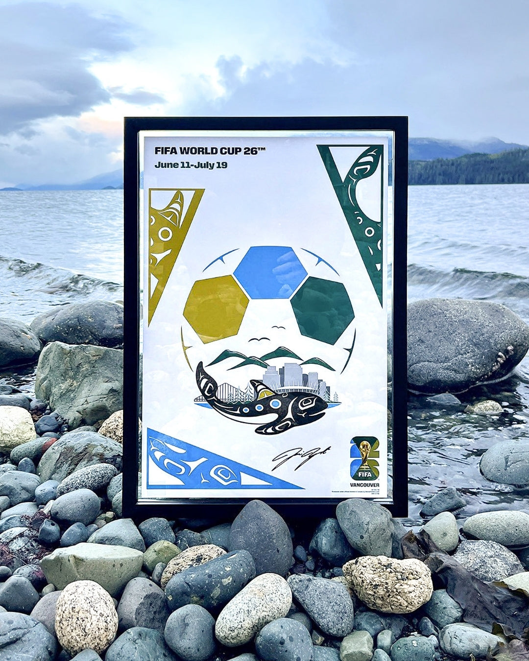Artwork for the FIFA World Cup 26 Host City Poster by artist Jamin Zuroski  in a black frame on the rocks of a Vancouver BC beach.