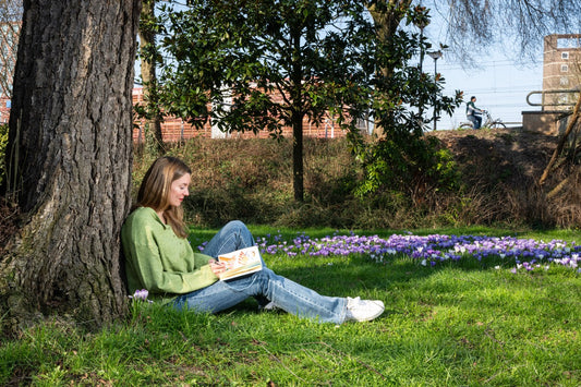 A woman sitting next to a tree creating in her sketchbook.