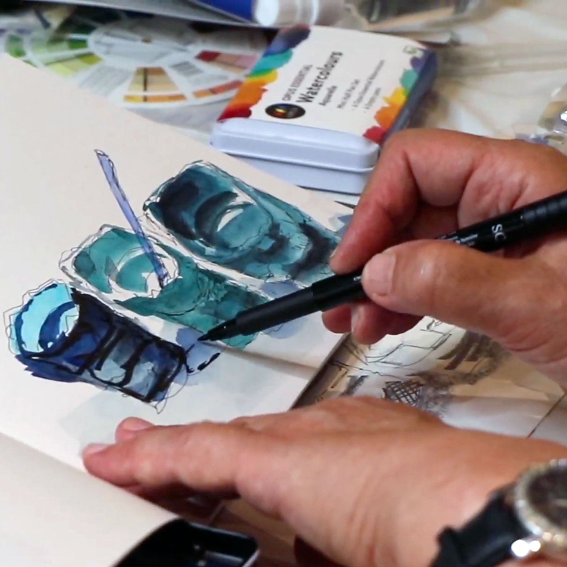 Two hands drawing and using watercolour