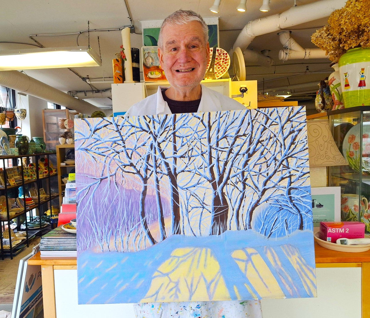 A man holds his painting of a snowy landscape with trees