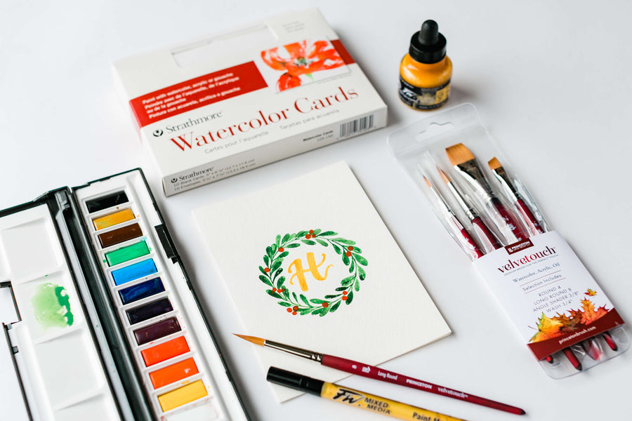 a handpainted holiday card with the paints and brushes used to create it