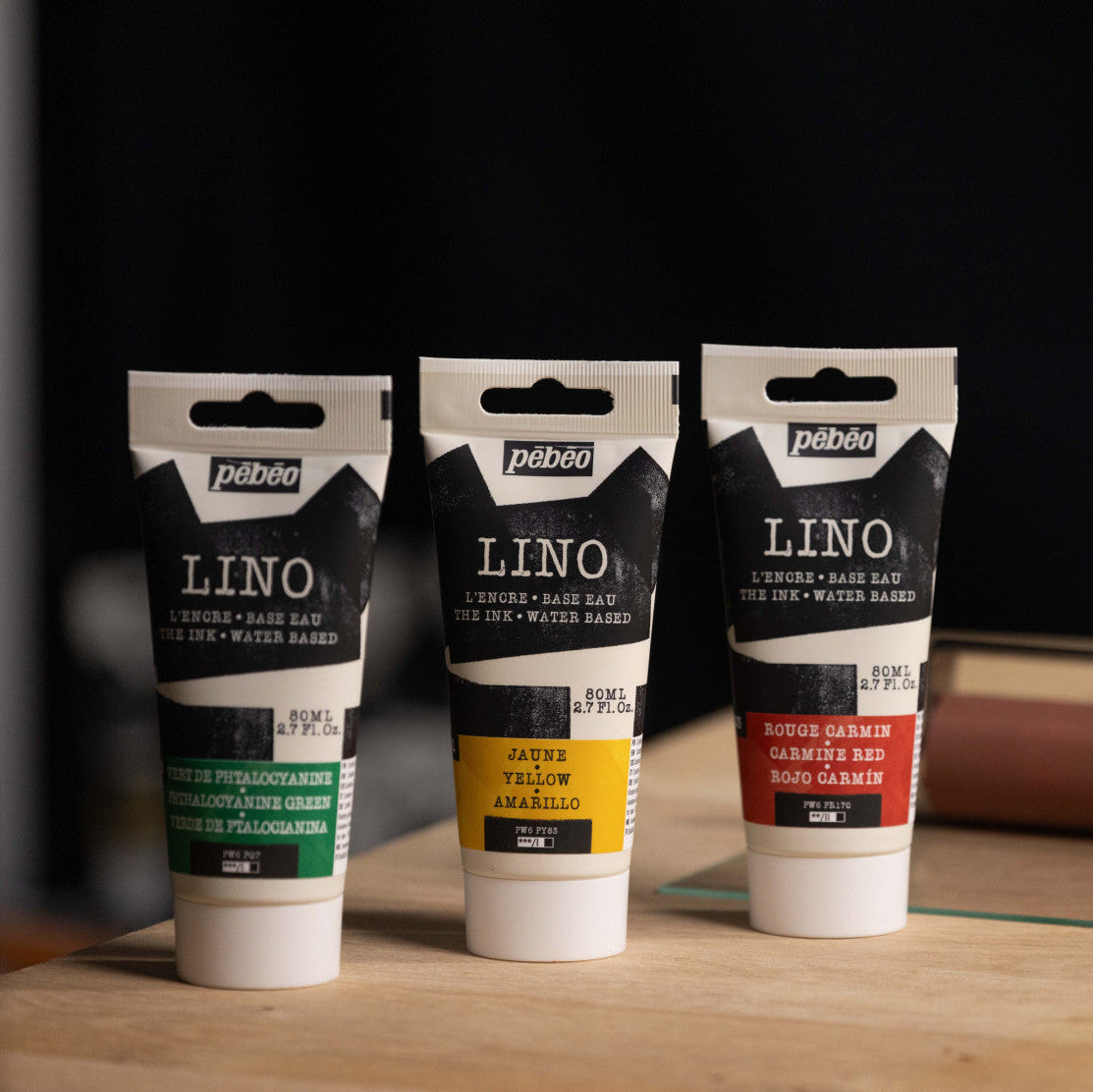 Three tubes of Pébéo Lino Ink on a wooden surface with a dark background