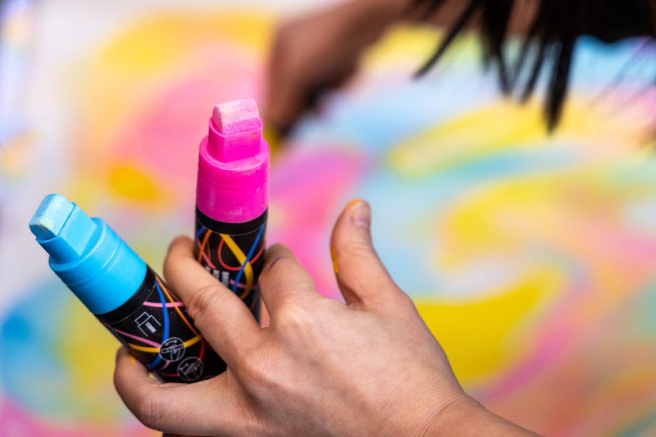 Hand holding two colorful spray bottles against a multicolored abstract background