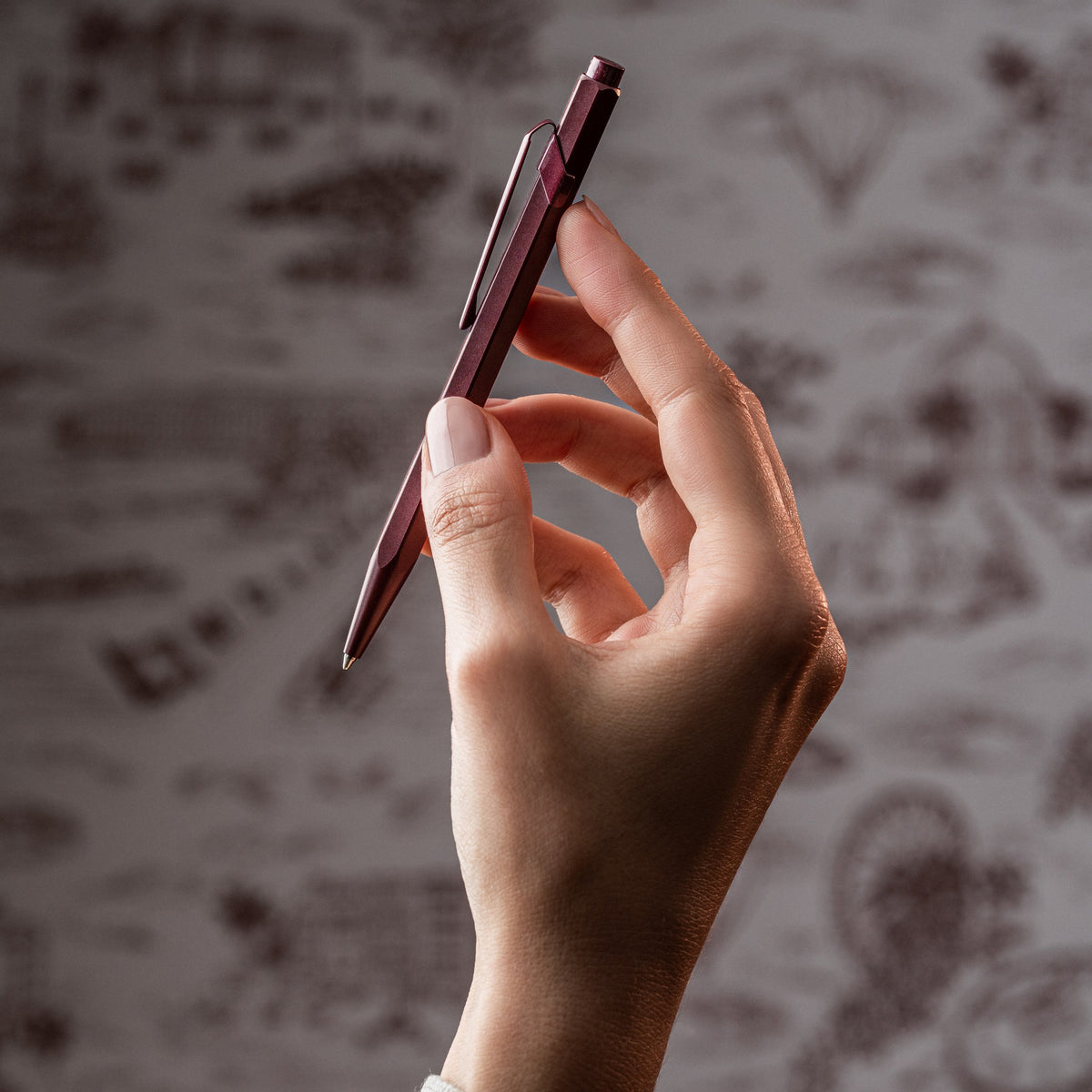 Hand holding the Caran d'Ache Toile de Jouy 849 ballpoint pen in burgundy