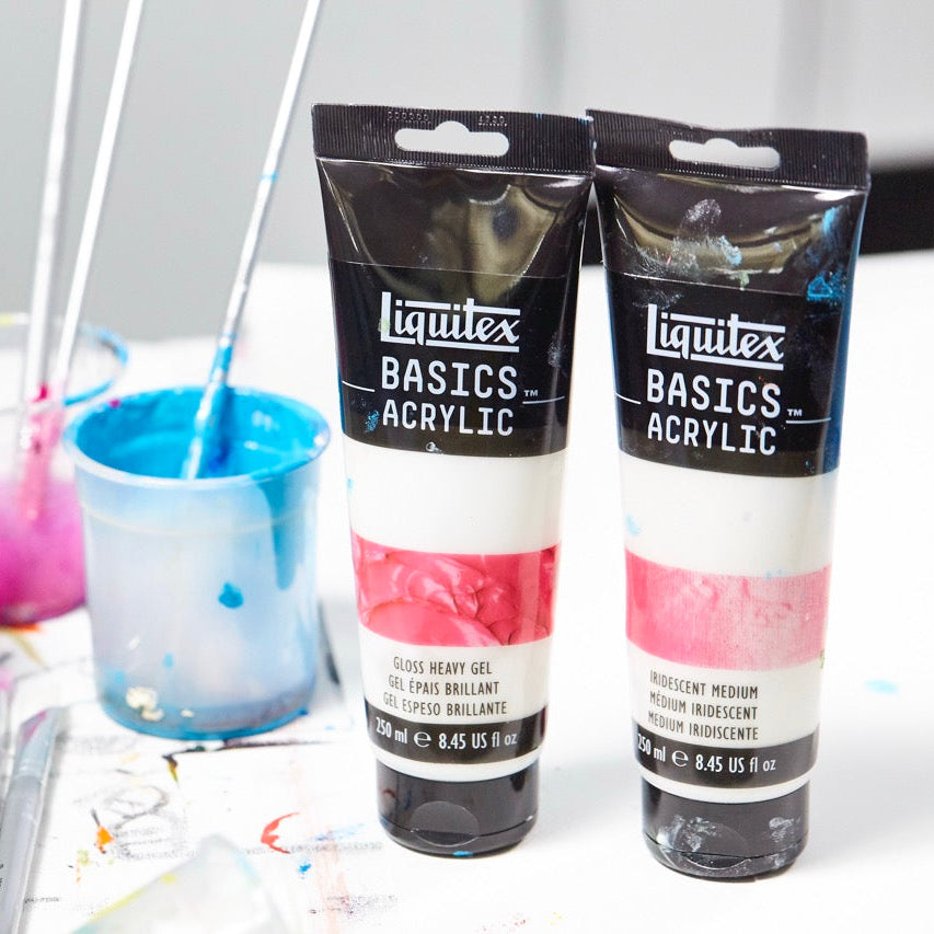 Two tubes of Liquitex Basics Acrylic paint with paintbrushes and cups on a white surface.